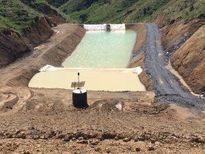 Sediment retention pond in steep hill country, with a flow-activated flocculent dosing system in the foreground (Source: RST Solutions Limited).